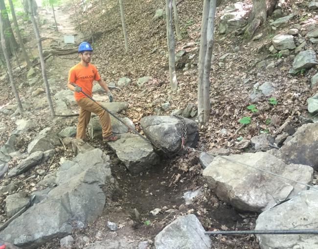 Crew member using a rock bar and a grip hoist to set a stepping stone.  